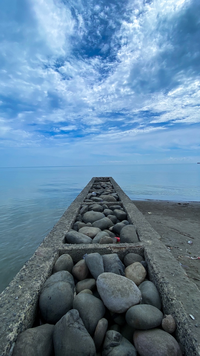 Pile of stones on the beach with blue sky and clouds in the background